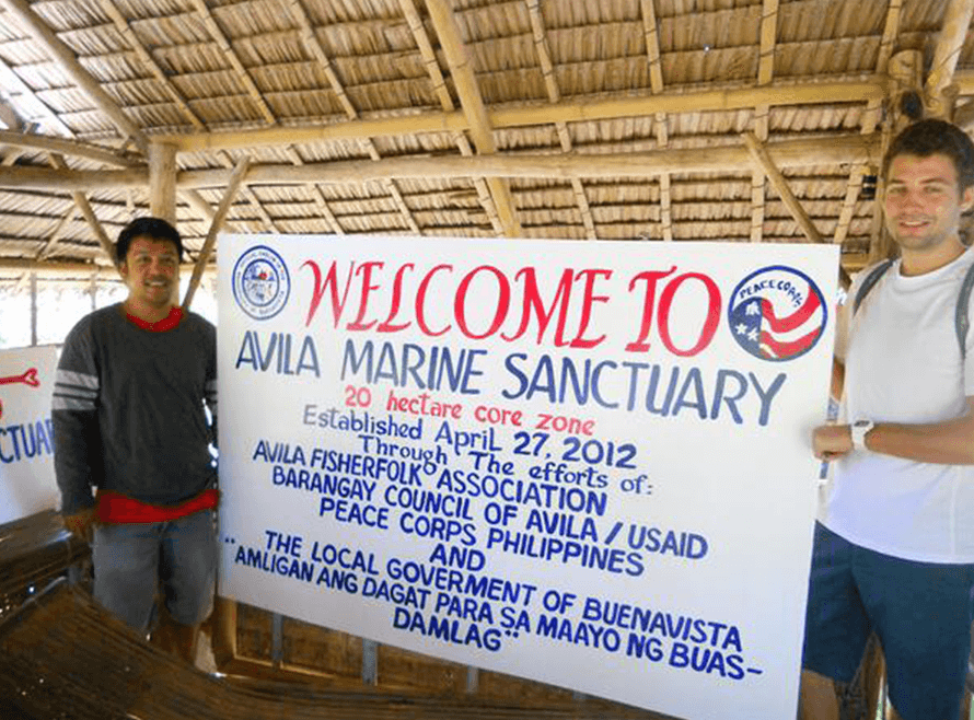 Two men stand next to a welcome sign in Guimaras, Philippines